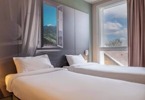 Habitación de hotel con dos camas, un ventanal grande con vista a las montañas y un diseño moderno.