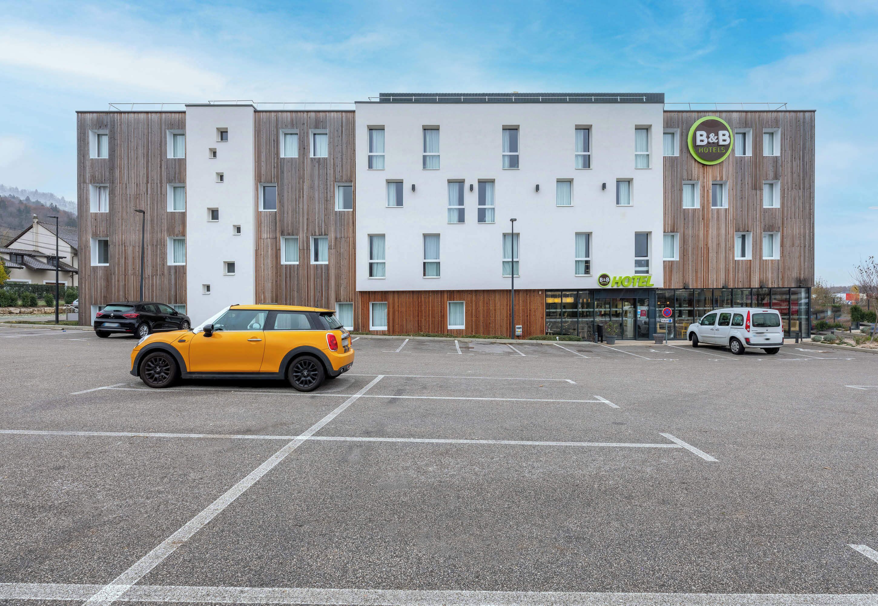 Un hotel B&B moderno con fachada blanca y detalles de madera, que cuenta con un estacionamiento y dos automóviles.