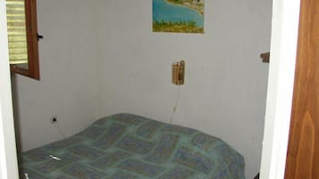Un dormitorio con una colcha estampada, un cuadro de un paisaje en la pared y una lámpara de noche.