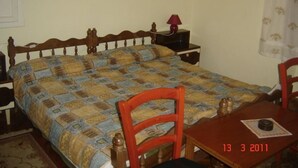 A bedroom with a wooden bed, a nightstand with a lamp, a chair, and a table with a book. - Impact villas (Rasa)