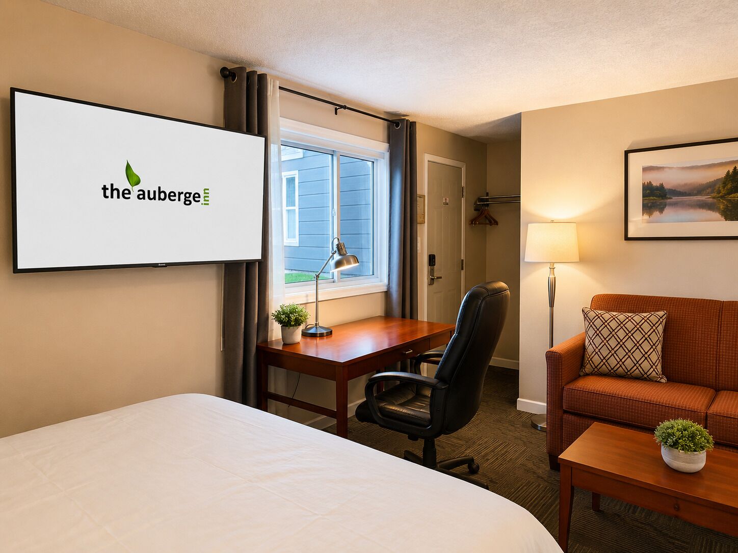 A hotel room with a bed, a desk with a chair, a sofa, a lamp, and a window with curtains.