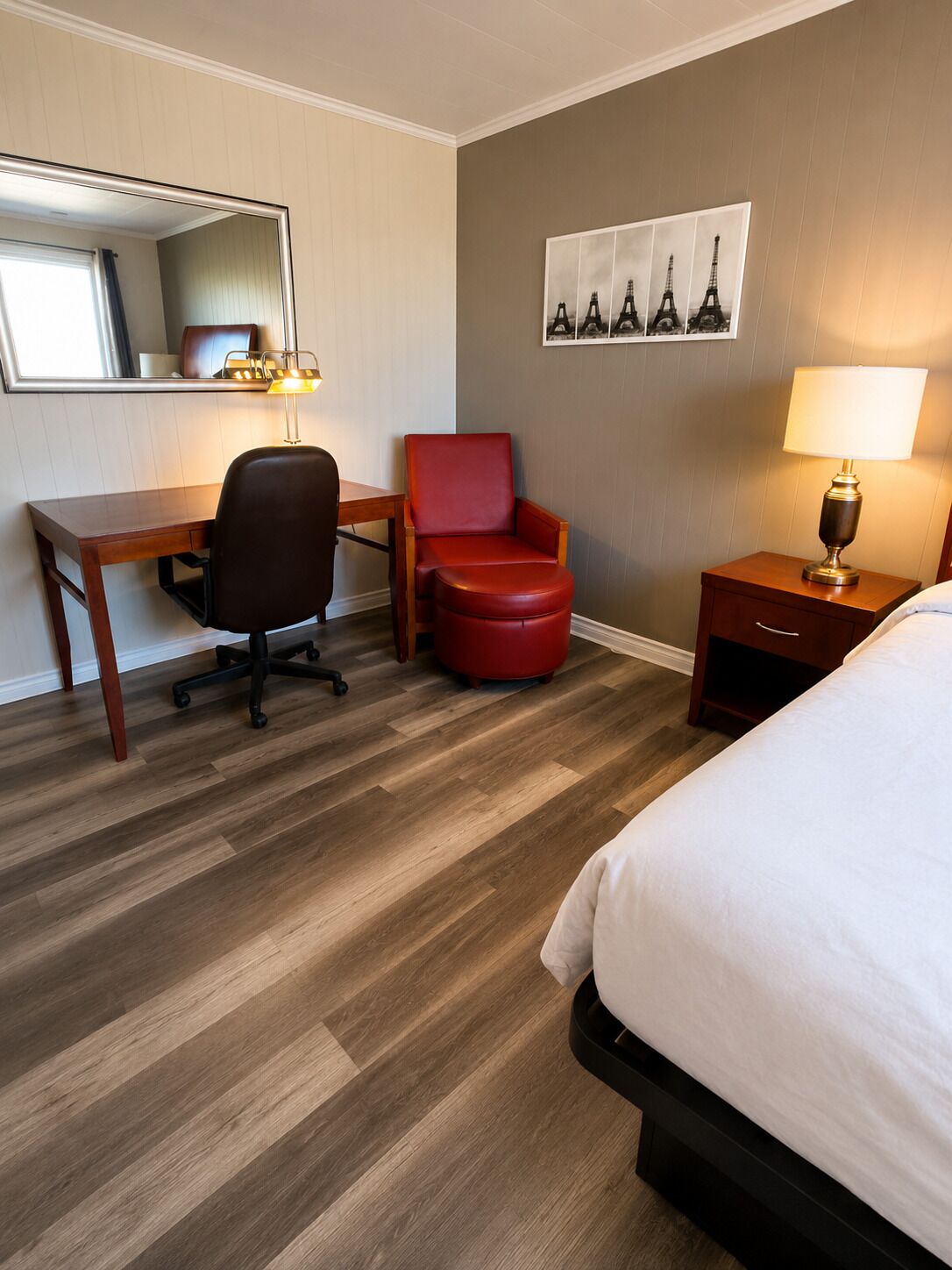 Habitación de hotel con cama, escritorio, silla, mesita de noche, lámpara y un cuadro en la pared de la Torre Eiffel.