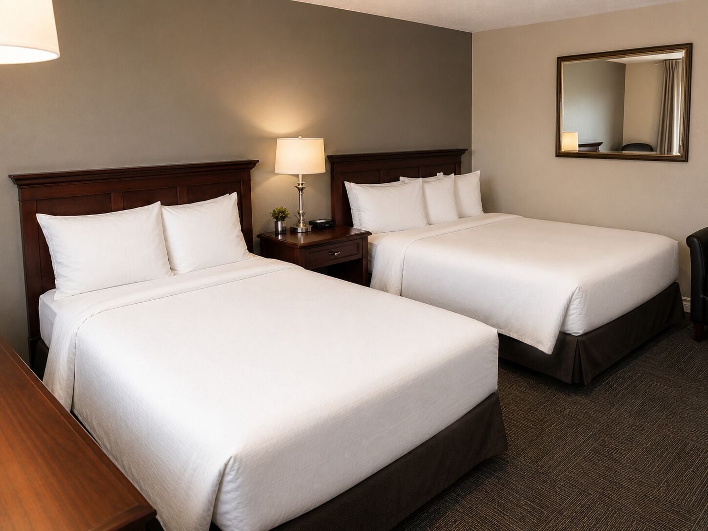 A hotel room with two beds, a nightstand, a lamp, and a mirror.
