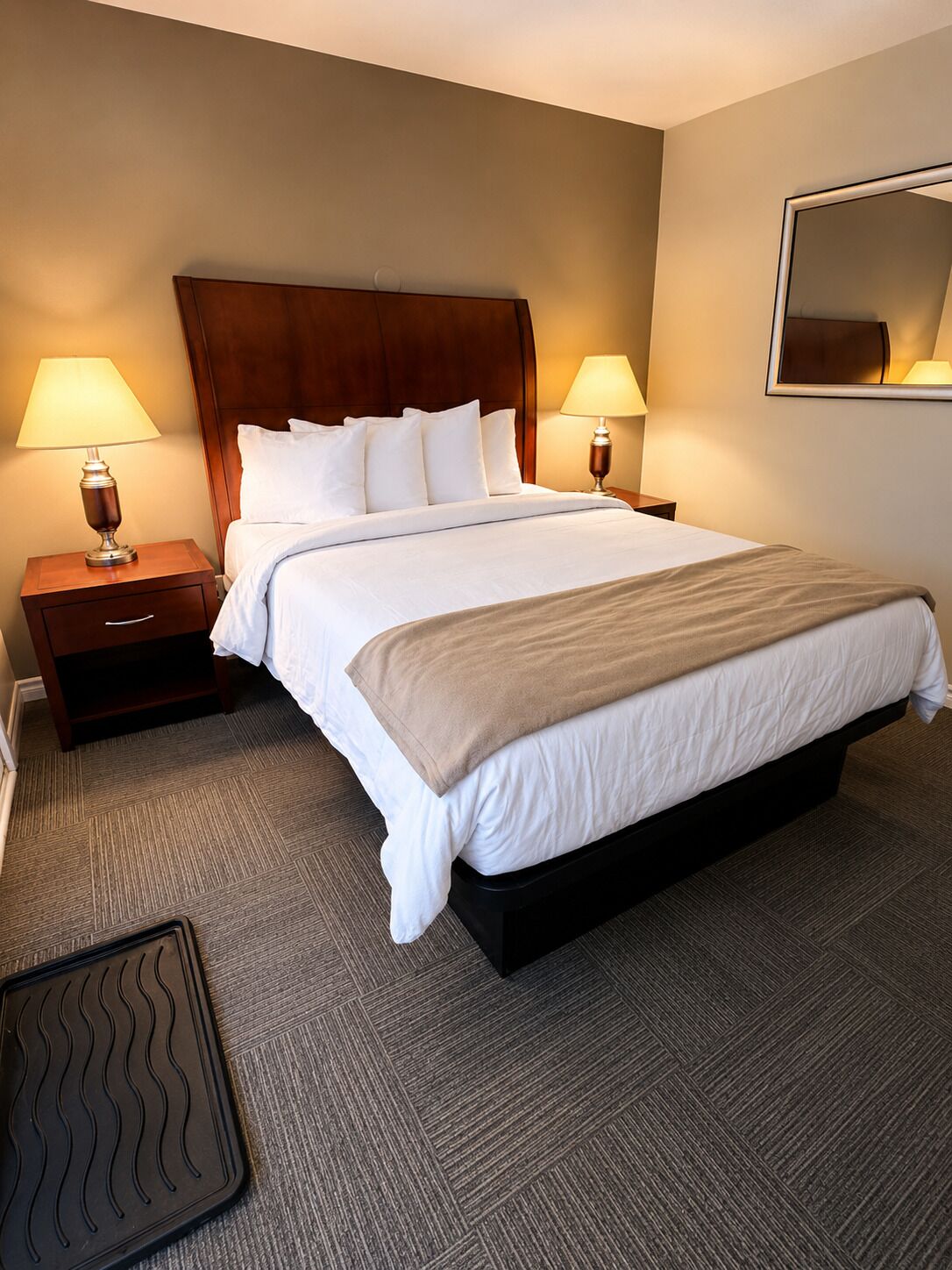 A hotel room with a large bed, two bedside tables, a headboard, and a wall-mounted mirror.