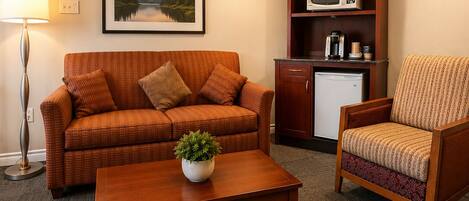 A living room with a sofa, armchair, coffee table, and a microwave.