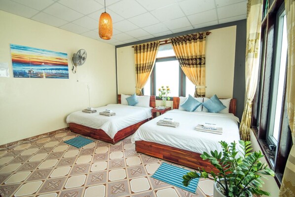 A hotel room with two beds, a large window with curtains, a wall-mounted fan, a painting, and a patterned floor.