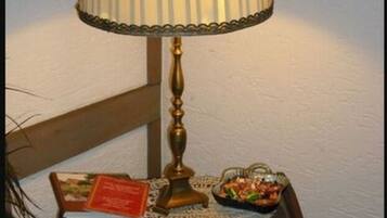 A table with a lamp, a bowl of snacks, and a book on a wooden table against a white wall.