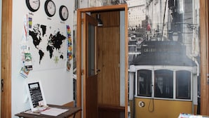 A room with a world map, clocks, a tram, and a wooden door. - TripGeo Guesthouse (Lisbon)