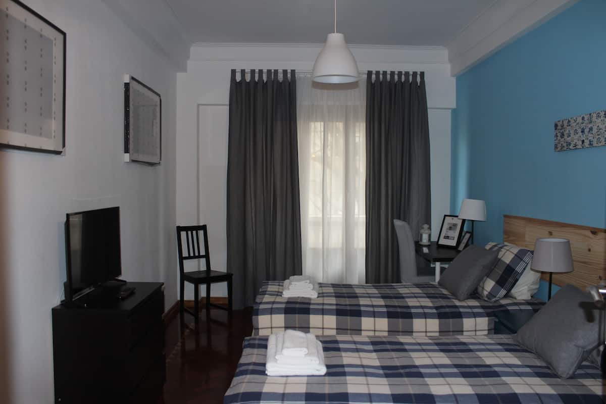 Una habitación de hotel con cama, escritorio, silla, televisor y cortinas.