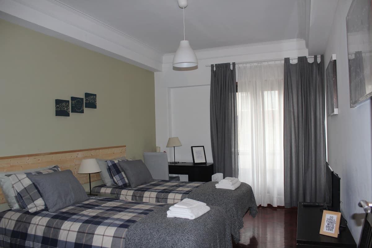 Habitación de hotel con dos camas, un escritorio, una silla, una lámpara y un marco de fotos en la pared.
