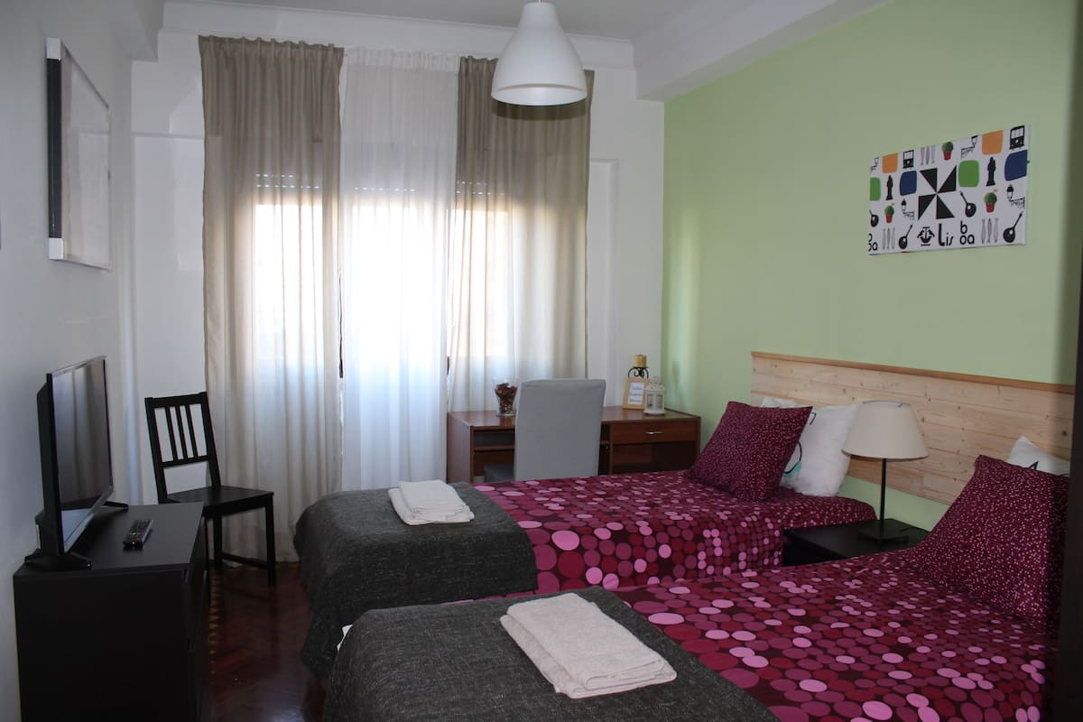 Habitación de hotel con dos camas, un escritorio con computadora, una silla y una ventana con cortinas.