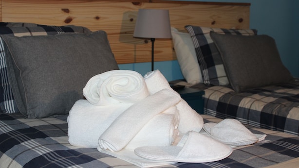 A bed with a plaid bedspread, a lamp, and neatly folded towels and slippers. - TripGeo Guesthouse (Lisbon)