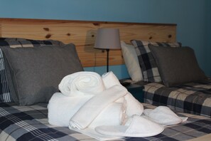 A bed with a plaid bedspread, a lamp, and neatly folded towels and slippers. - TripGeo Guesthouse (Lisbon)