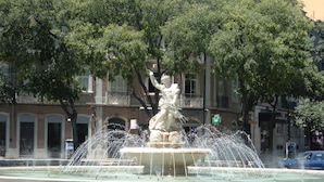 A fountain with a statue in the center, surrounded by a paved area and trees. - TripGeo Guesthouse (Lisbon)