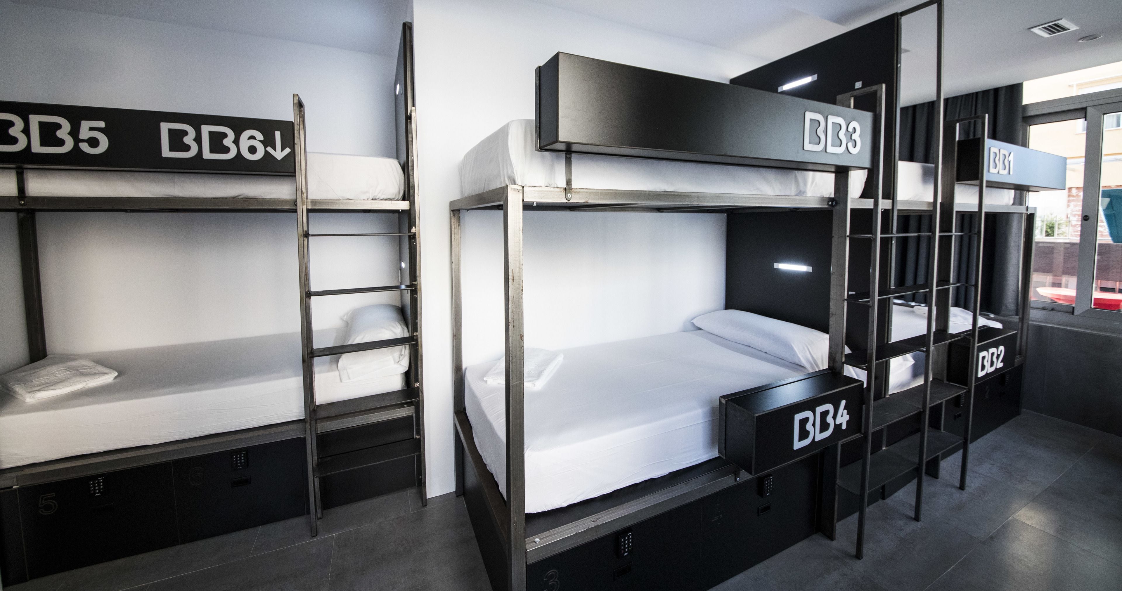 A dormitory-style room with bunk beds labeled BB5, BB6, BB3, BB4, and BB2. Each bed has a ladder and a small storage drawer.