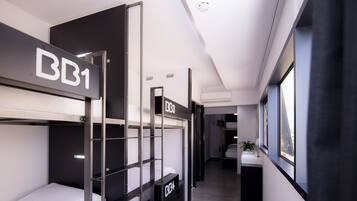Una habitación de hotel moderna con literas identificadas como BB1 y BB3, un baño con lavamanos y espejo, y vistas por una ventana.