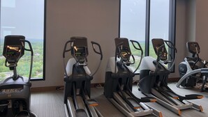 A row of stationary bikes in a room with large windows, a treadmill, and a rowing machine. - New World Stay (McLean)
