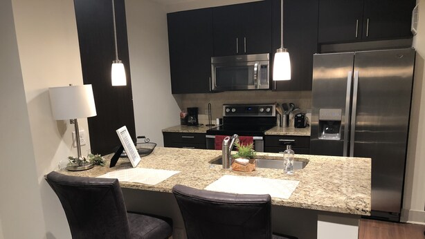 A modern kitchen with dark cabinets, stainless steel appliances, and a granite countertop. - New World Stay (McLean)