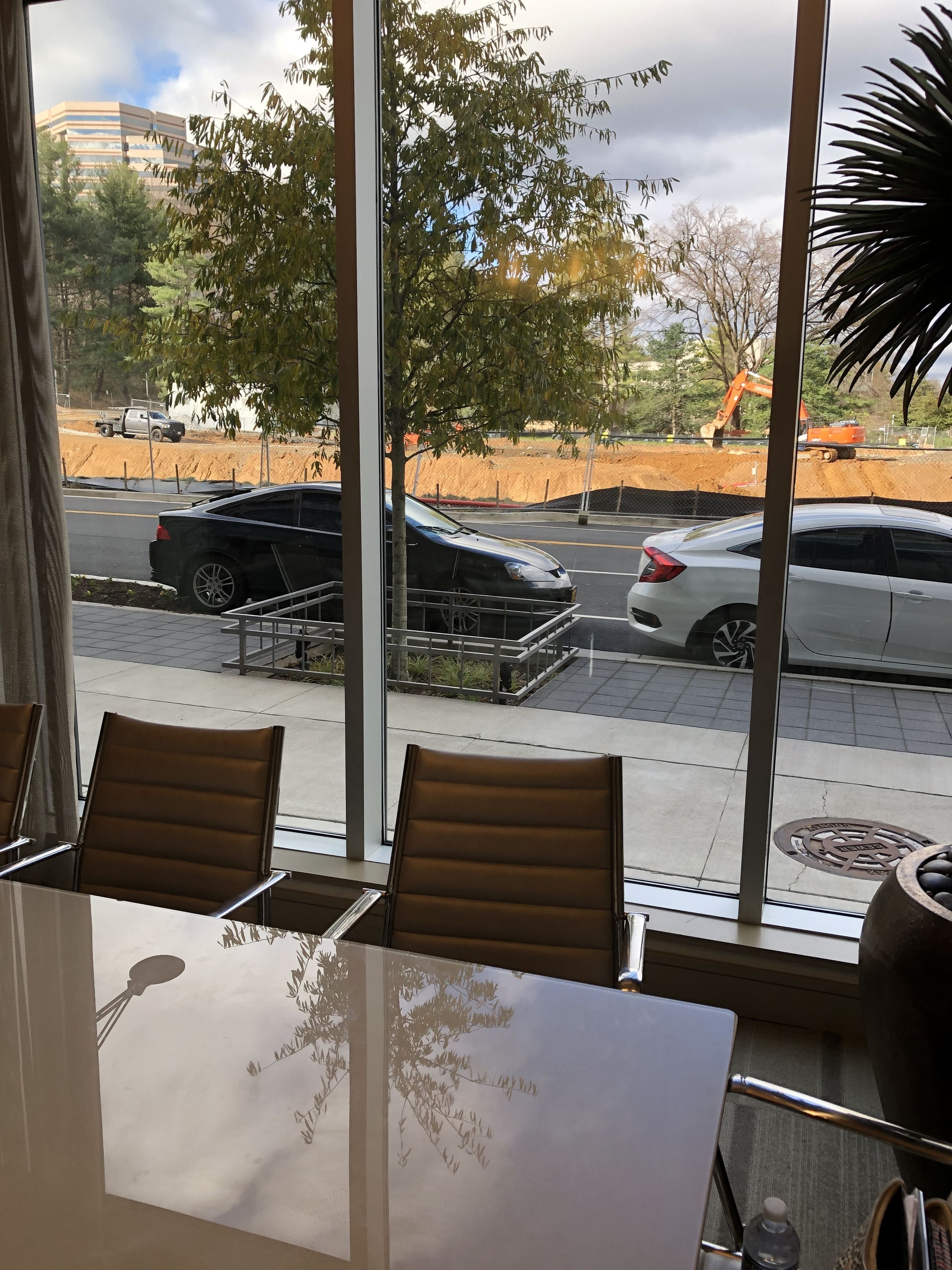 A hotel room with a large window offering a view of the street and construction site. There are two chairs and a table in the room.