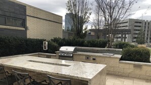 An outdoor kitchen area with a marble countertop, a grill, and bar stools. - New World Stay (McLean)