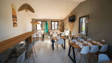 A modern dining area with long wooden tables, white chairs, and pendant lighting.
