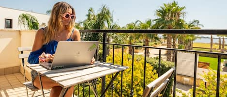 A person sitting at a table with a laptop on a balcony overlooking a garden with palm trees.