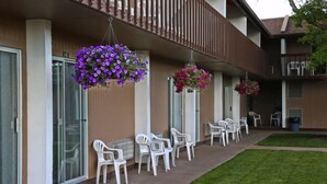 Un immeuble doté d’un balcon, de chaises en plastique blanches et de jardinières suspendues.
