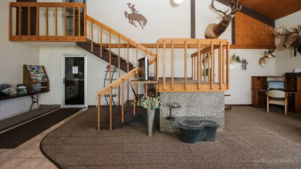 Une pièce spacieuse avec un escalier en bois, une tête de cerf accrochée au mur et la silhouette d’un cowboy peinte sur le mur.