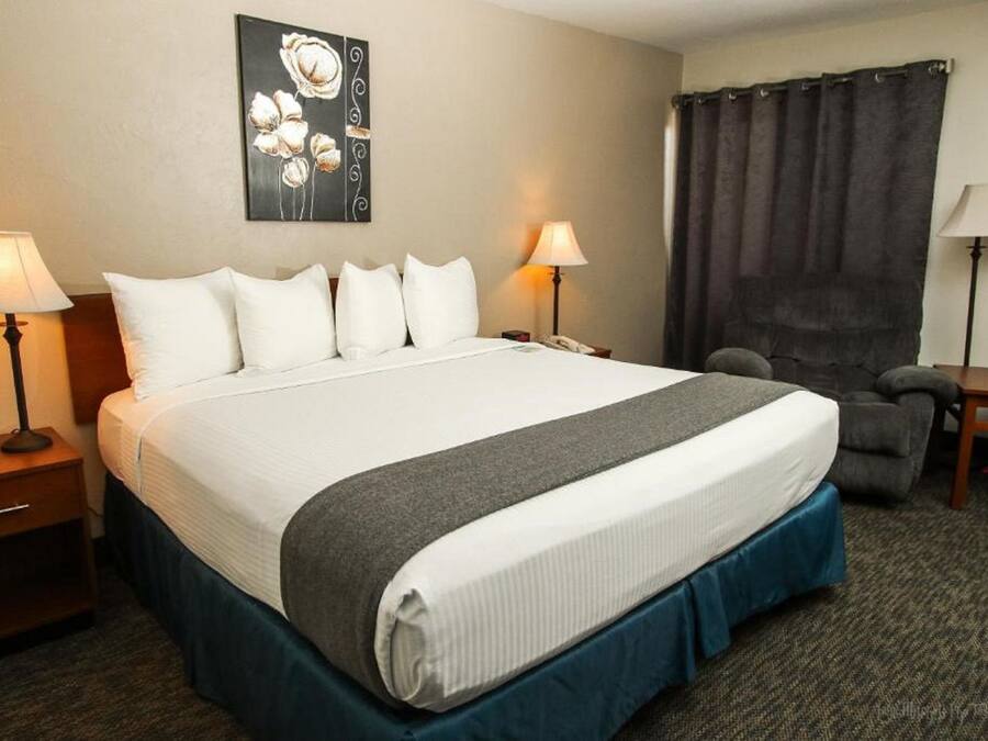 Una habitación de hotel con una cama grande, dos lámparas de noche, una silla, un escritorio y un cuadro en la pared.
