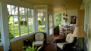 Una habitación iluminada por el sol, con ventanas amplias, muebles de mimbre y una zona de comedor con mesa y sillas.