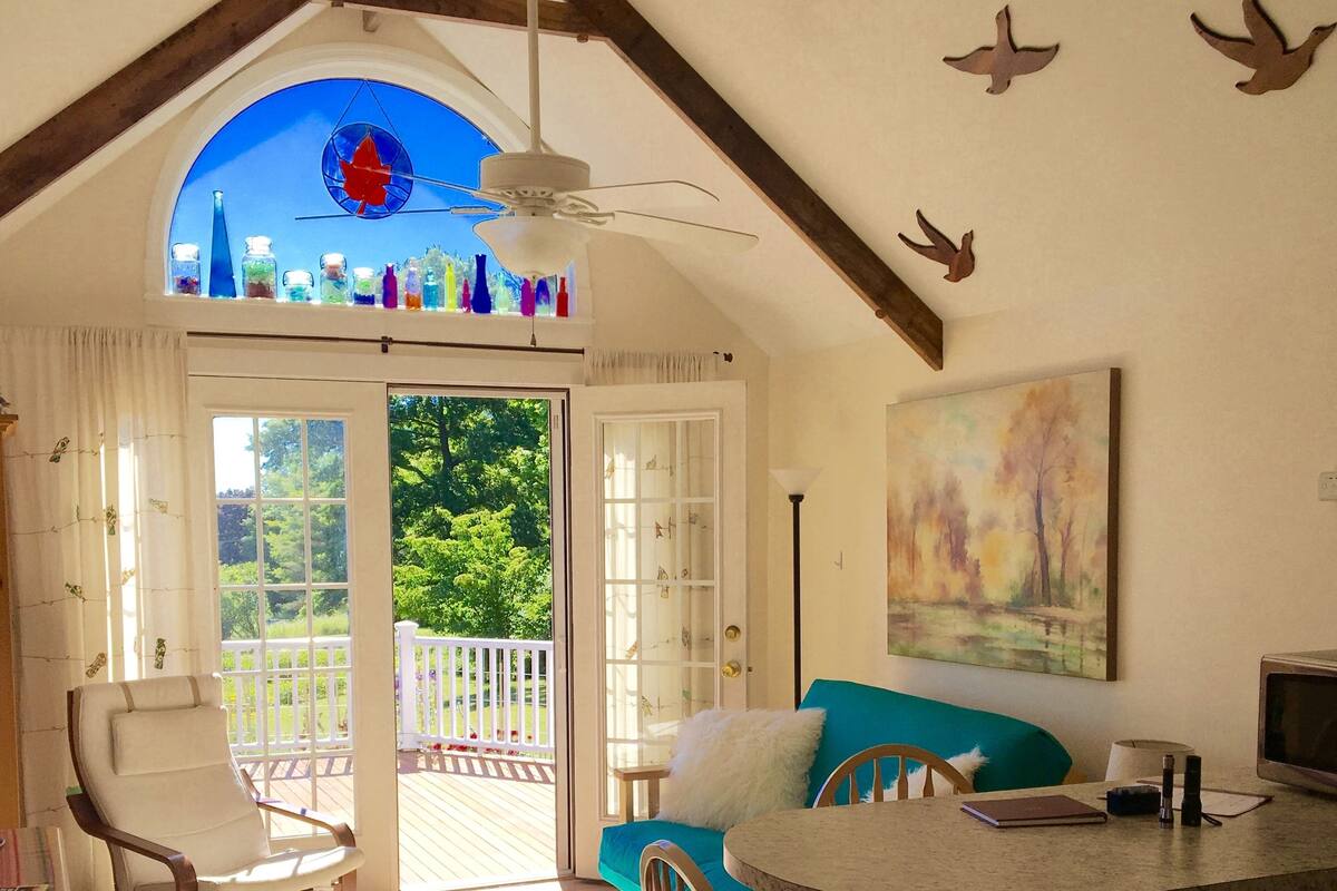 A cozy room with a balcony, a sofa, a chair, a table, and a painting on the wall.