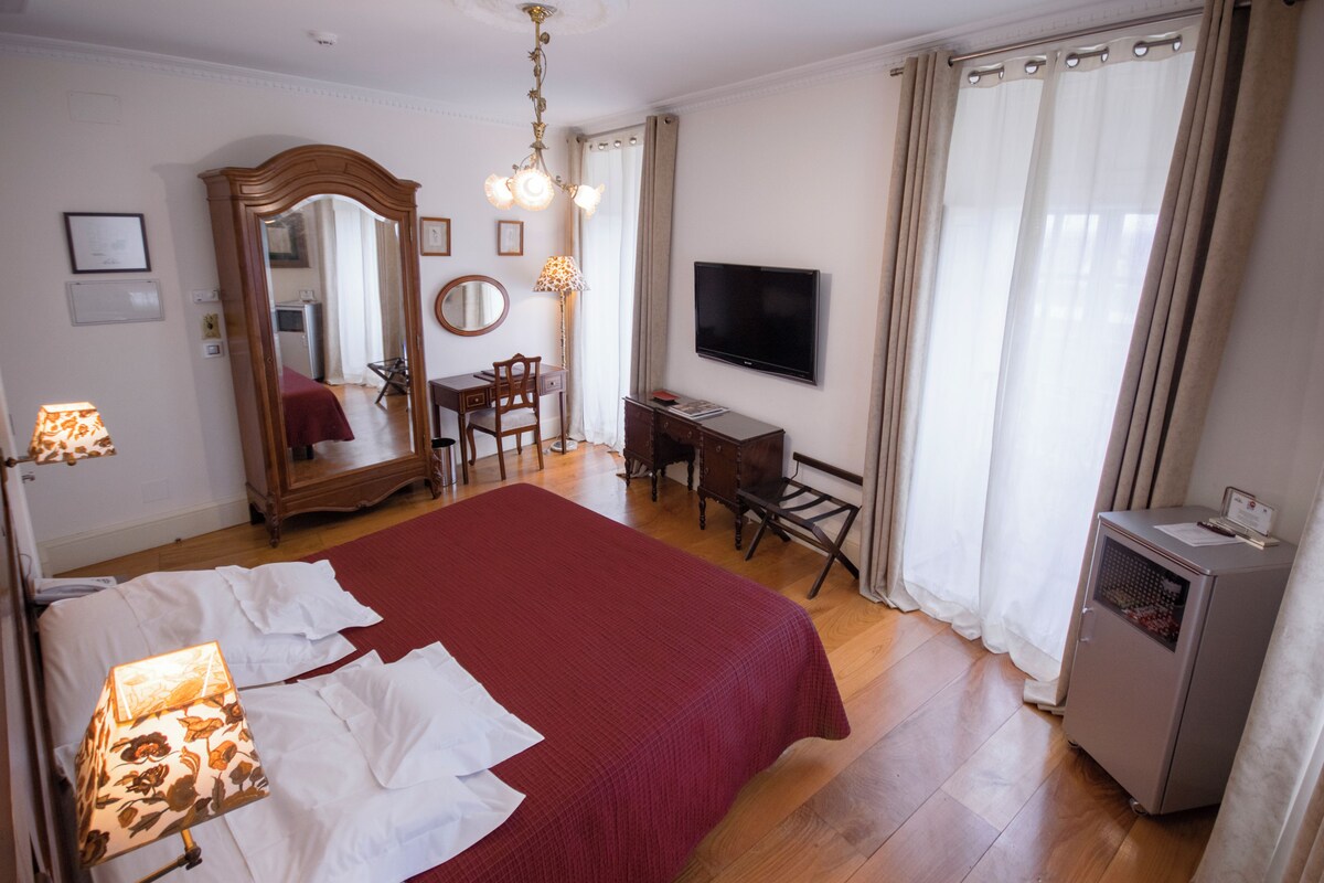 Ein Hotelzimmer mit einem großen Bett, einem Schreibtisch, einem Sessel, einem Fernseher und einer Minibar.