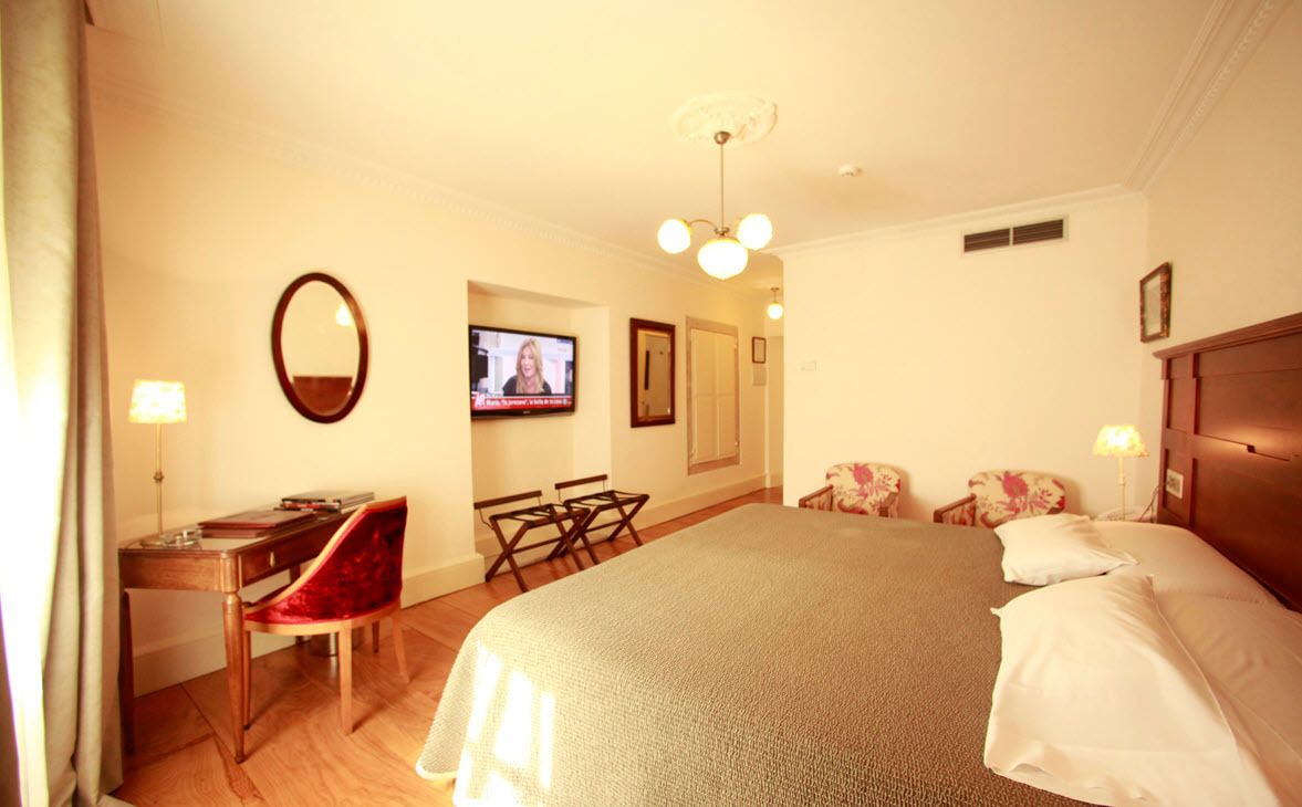 A hotel room with a bed, a desk with a chair, a television, and a mirror.
