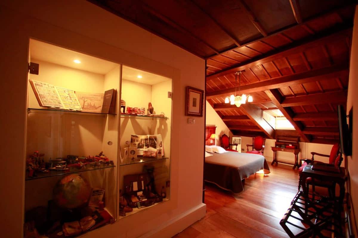 Ein Zimmer mit einer Glasvitrine, gefüllt mit verschiedenen Gegenständen, einem Bett mit weißer Bettdecke und Holzmöbeln.