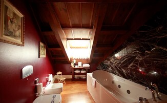 Un baño con una bañera grande, vigas de techo de madera, tragaluz y pared de mármol.