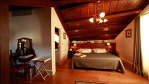 Une chambre confortable avec un plafond en bois, un lit recouvert d’une couverture grise, des lampes de chevet et un bureau agrémenté d’un miroir et de livres.
