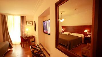 A hotel room with a bed, a desk with a chair, a television, and a large mirror.