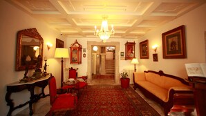 Un intérieur classique avec un lustre, des fauteuils rouges, un canapé et des tableaux encadrés accrochés aux murs.