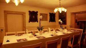 Une longue table à manger entourée de chaises, un lustre, des tableaux encadrés accrochés au mur et une porte au fond.