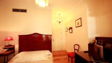 A hotel room with a wooden bed, a desk with a lamp, a chair, and a small table with a telephone.