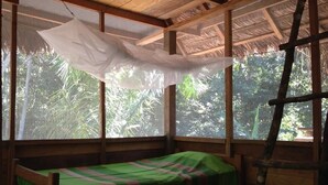 Una habitación pequeña con cama individual, colcha verde, ventanas amplias y una escalera de madera.