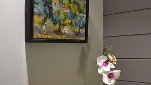 Un tableau encadré, une orchidée en pot, une bougie et un petit panier posés sur une étagère.