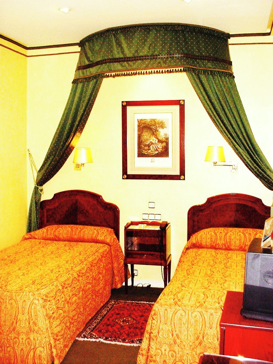 Une chambre d’hôtel avec deux lits simples, une table de chevet, une lampe et un tableau encadré au mur.