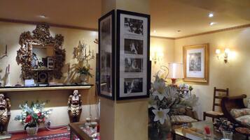 Un hall de hotel tradicional con decoración elaborada, incluyendo un espejo grande, fotografías enmarcadas y muebles clásicos.