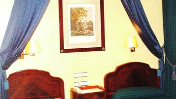 A hotel room with two beds, a nightstand, a framed picture on the wall, and a window with curtains.