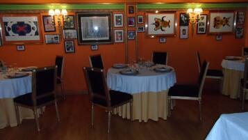 A dining area with round tables, chairs, framed pictures on the walls, and wall-mounted lamps.