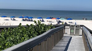 Une promenade en bois menant à une plage agrémentée de parasols bleus et de chaises longues.