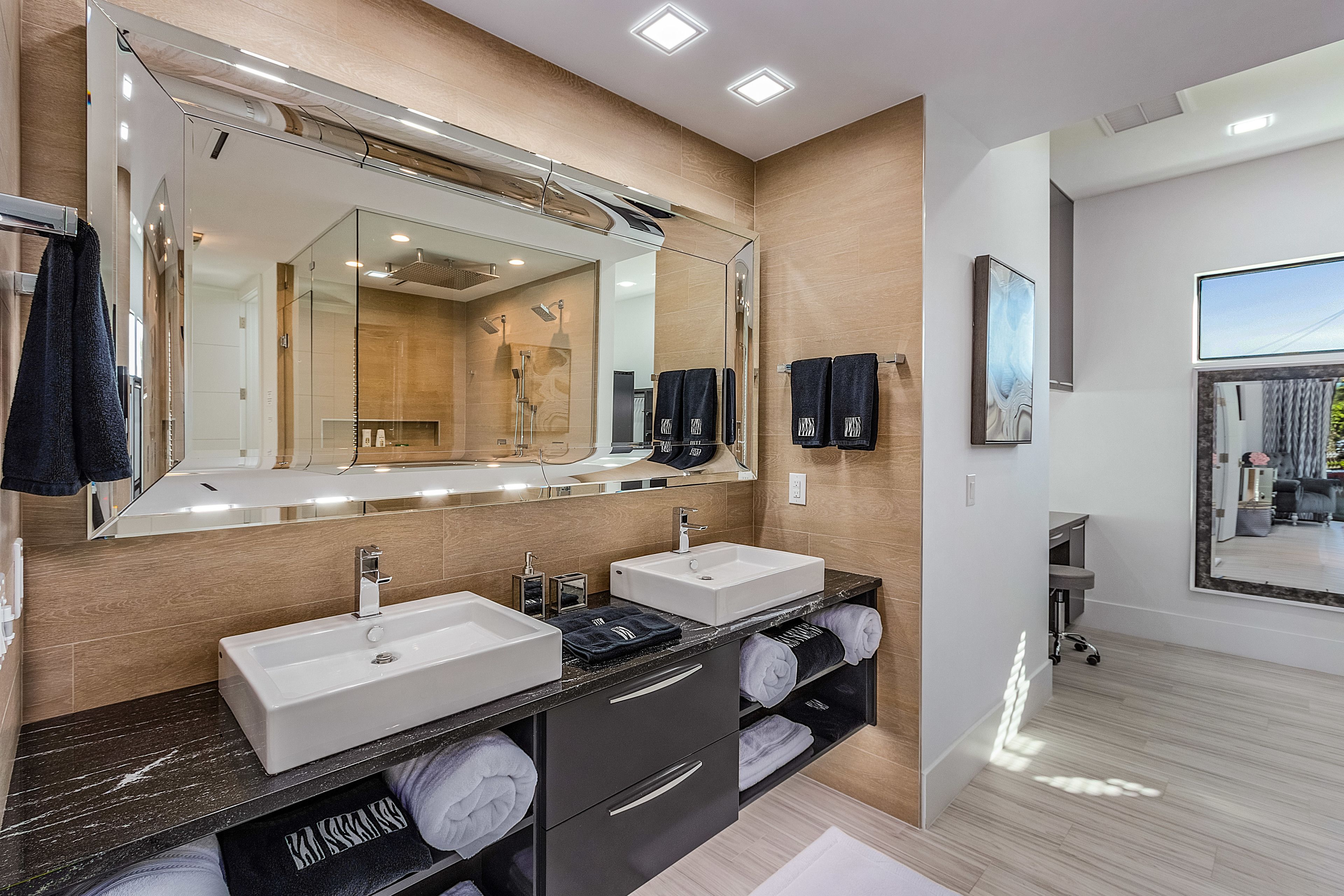 Une salle de bain moderne avec deux lavabos, un grand miroir et un meuble-lavabo doté de porte-serviettes.