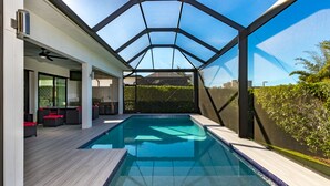 Une piscine intérieure moderne dotée d’un toit en verre, d’un bar avec des coussins rouges et offrant une vue sur l’extérieur.