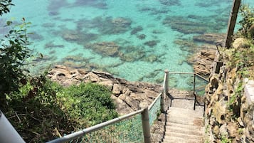Una escalera que desciende hacia una costa rocosa con agua turquesa transparente.